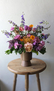 Modern flower arrangement with seasonal flowers. Arranged in a Mauve ceramic footed vase. Available for local flower delivery.  